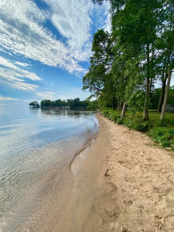 A view of a beautiful sandy beach on a sunny summer day, with clear blue water and a few small waves lapping at the shore.
