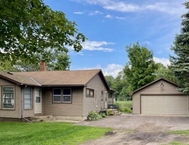 A picturesque summer front view of Cabin 1 at Sunset Shore Mille Lacs, featuring a cozy porch, and lush greenery.