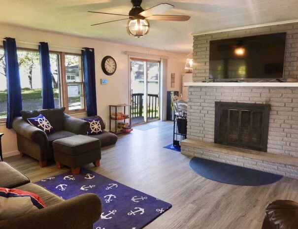 The family room in Cabin 1 at Sunset Shore Mille Lacs features a couch, chair, fireplace, open view into the kitchen and dining area, board game, and books.