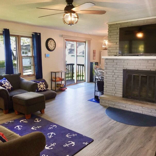 The family room in Cabin 1 at Sunset Shore Mille Lacs features a couch, chair, fireplace, open view into the kitchen and dining area, board game, and books.