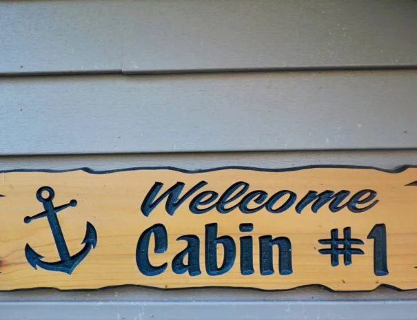 A wooden sign with the words "Welcome Cabin #1" and a carved anchor.