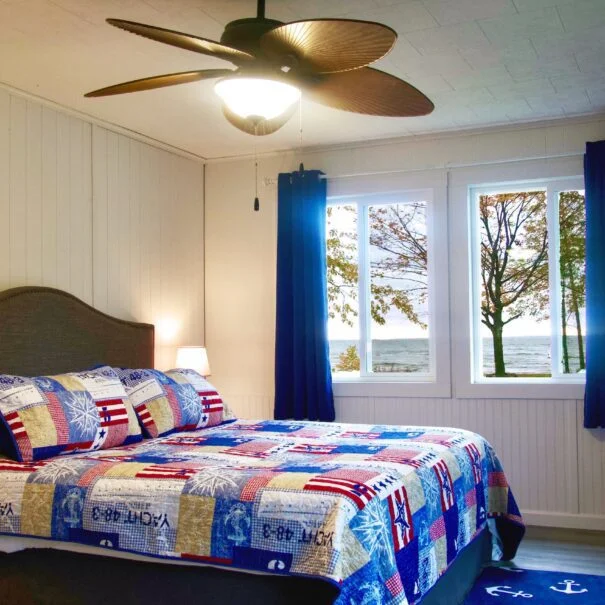The spacious main bedroom in Cabin 1 at Sunset Shore Mille Lacs features a king-size bed, channel and lake views, a workstation, and a TV.