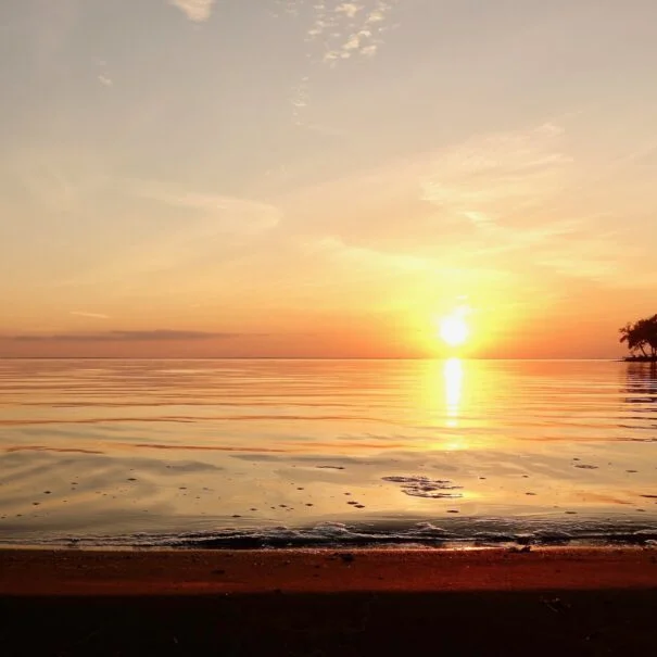 Sunset over calm lake, with orange and pink hues reflecting in the glasslike water